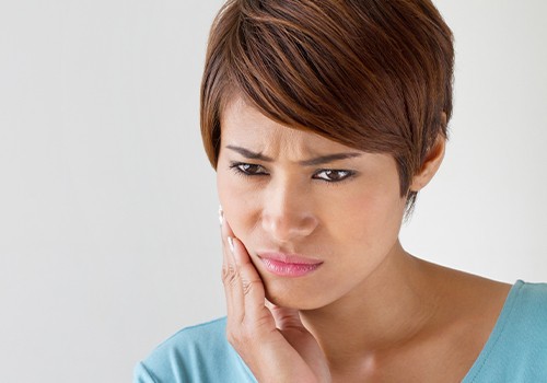 Woman in need of restorative dentistry holding jaw