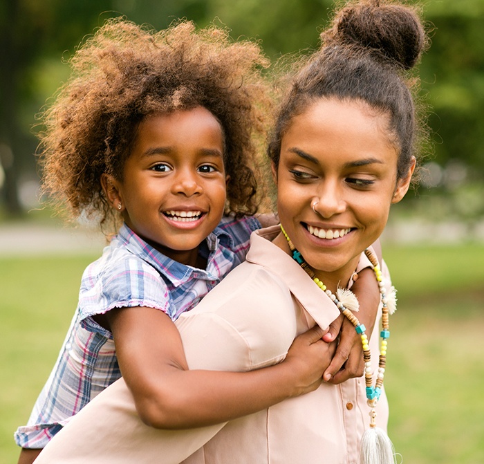 Daughter with healthy smile after children's dentistry getting a piggy back ride from mom