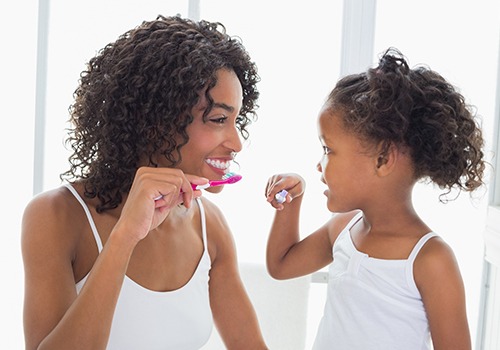 Mother showing daughter how to brush teeth