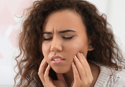 Young woman in need of wisdom tooth extraction holding jaw