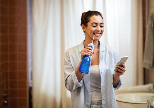 Woman water flossing while using her phone