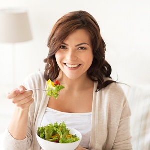 Woman smiling while eating a bowl of salad