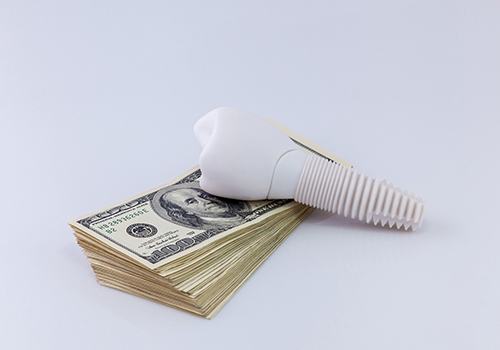 Model implant and money representing cost of dental implants in Kerrville 