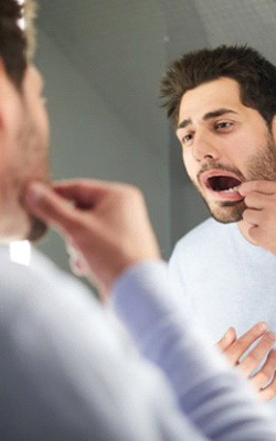 Man checking for gum disease in bathroom mirror
