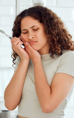 Woman holding her aching jaw after brushing her teeth