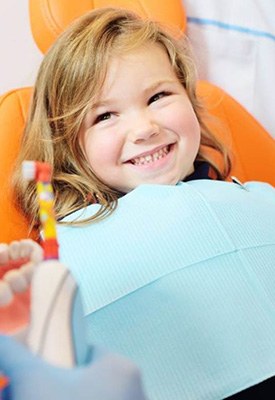 Child smiling in patient’s chair while dentist holds a dental model