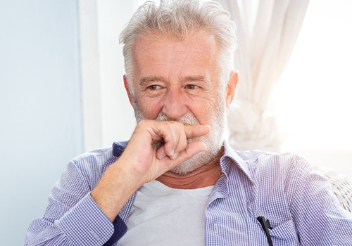 Older man in need of tooth replacement covering his smile
