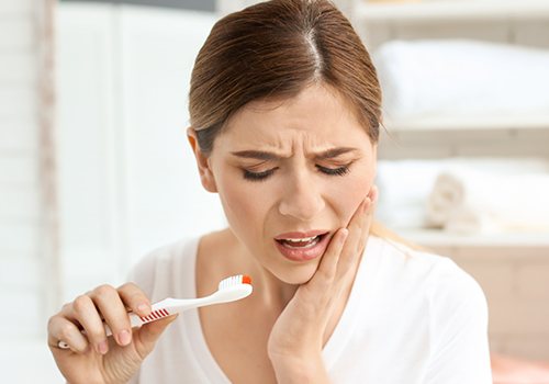 Woman holding jaw with blood on toothbrush in need of gum disease treatment