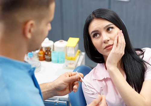 woman holding mouth in pain in dental chair 