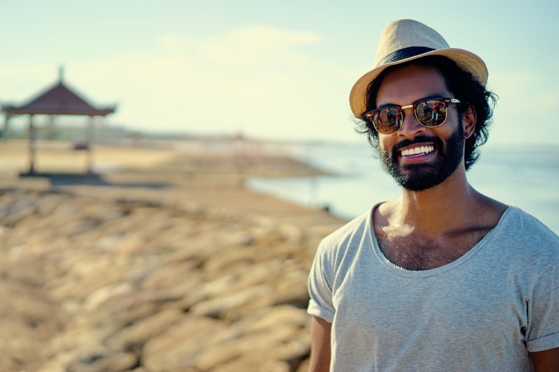 a man wearing a hat while standing on the beach and showing his porcelain veneers