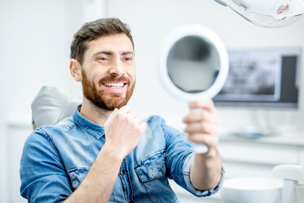 A man in a dental chair smiling at himself in the mirror.