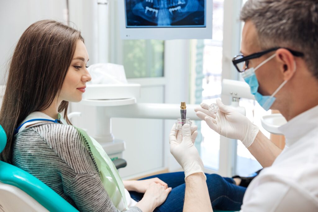 Dentist showing large model implant to woman in dental chair