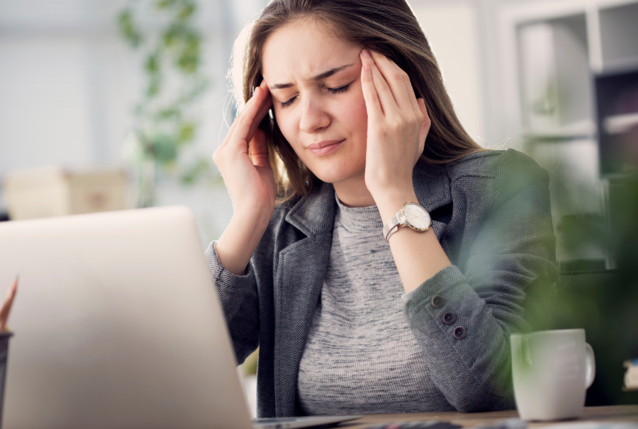 Woman at desk with laptop, holding temples in pain